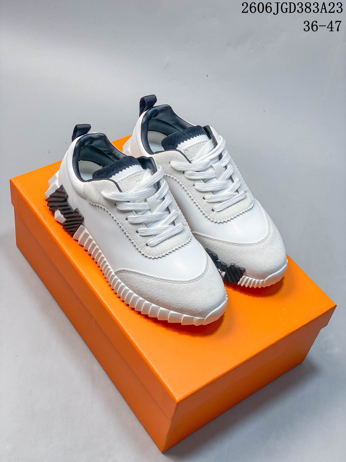 Pair of white low-top sneakers with black accents and ridged soles on an orange box
