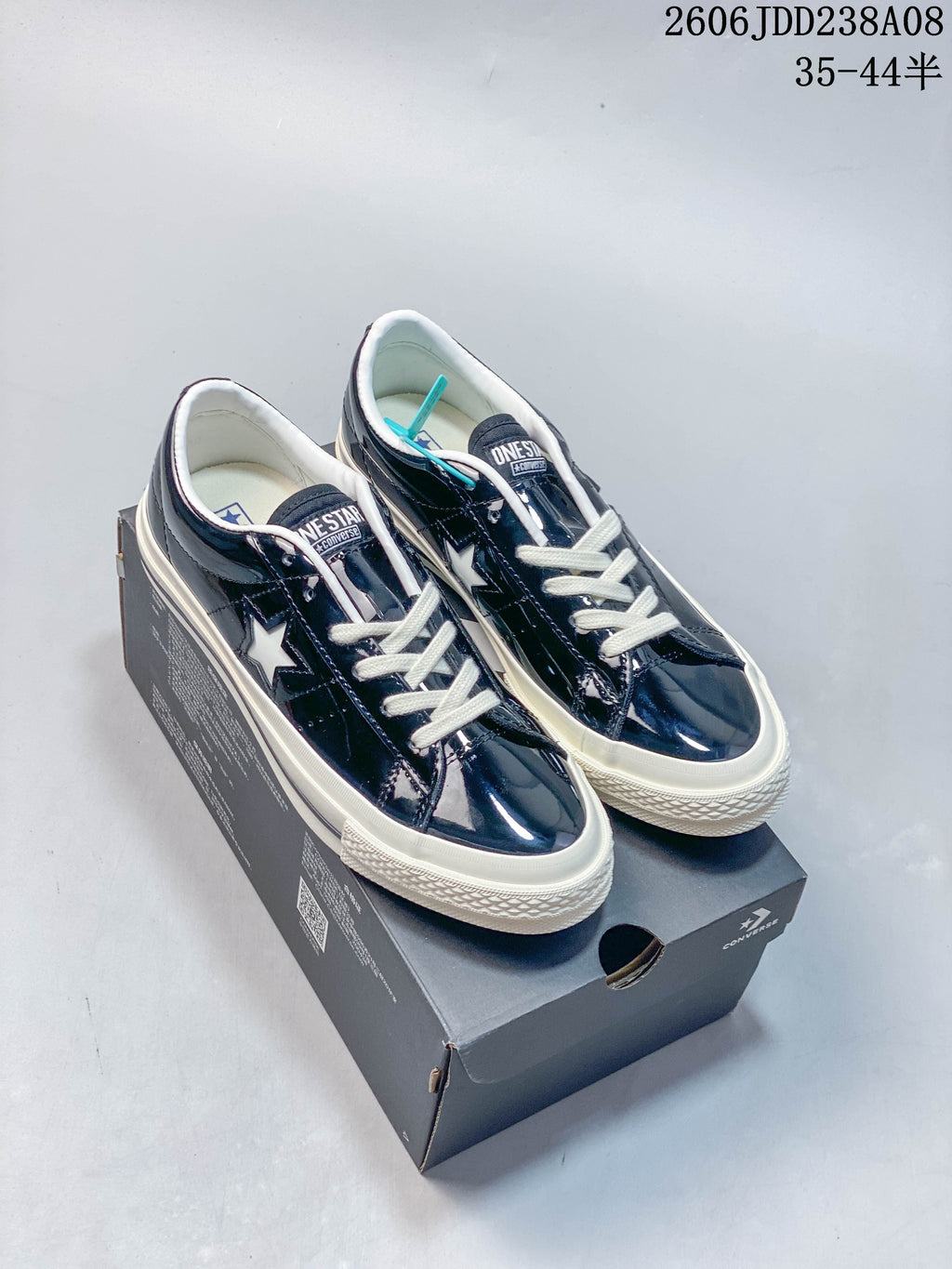 Pair of glossy navy Converse One Star low-top sneakers with white laces and off-white soles, shown on a shoebox.