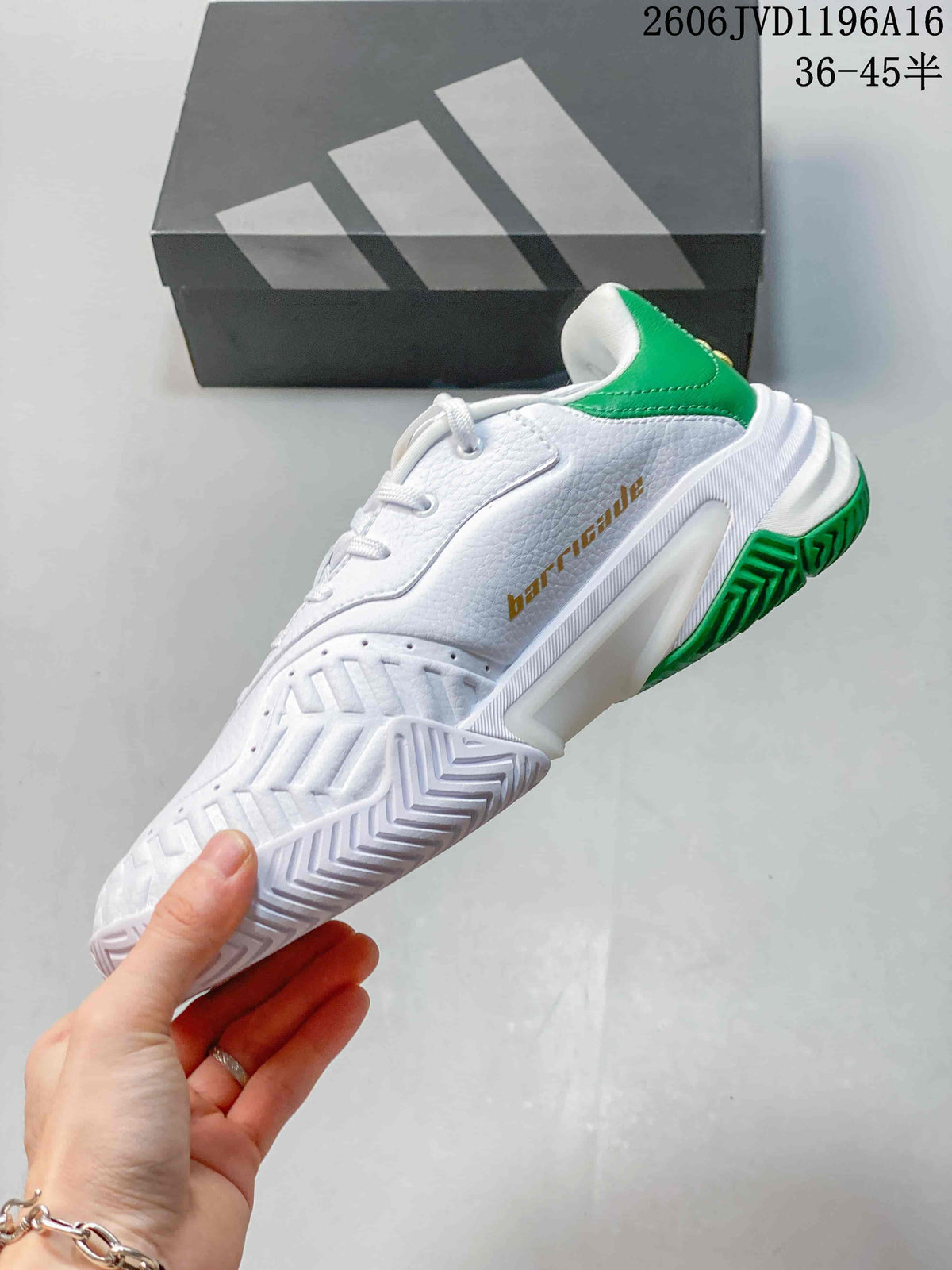 Side view of the white tennis shoe with green outsole accents and gold-tone Barricade lettering.