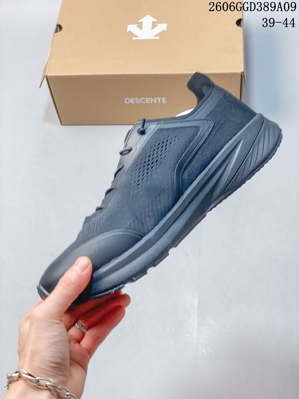 Side profile of a dark gray Descente running shoe with perforated panels and a thick sole.