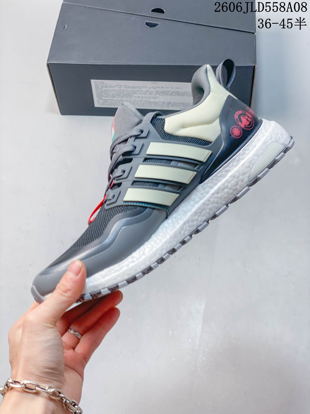 Side view of a grey Adidas shoe with pale side stripes, coral accents, and a white midsole.