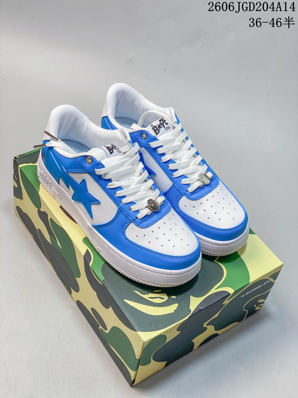 Blue and white BAPE STA low-top sneakers with perforated toes and white laces on a camouflage-patterned box