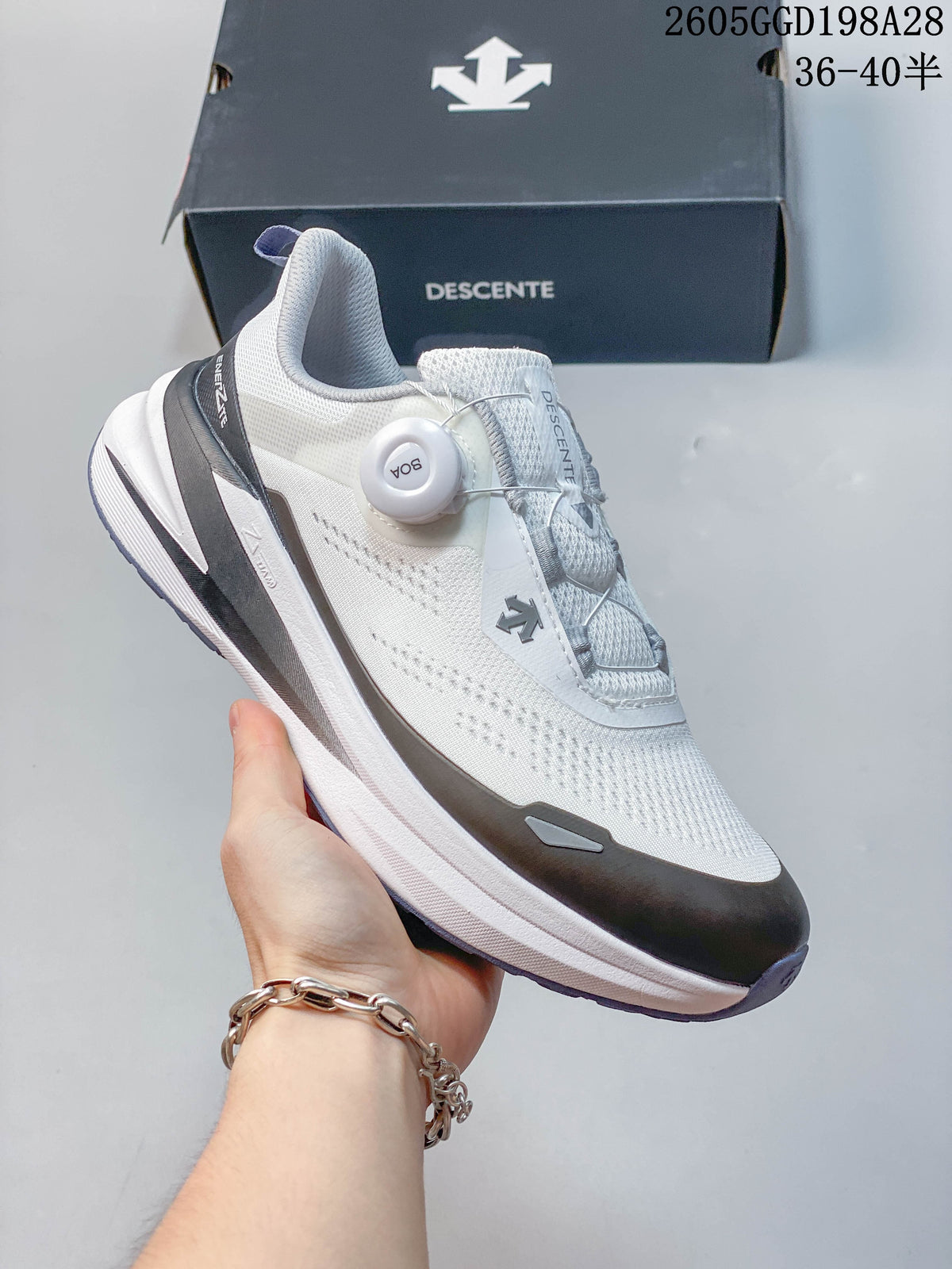 Angled view of the white Descente running shoe with dark gray overlays and blue-violet outsole accents; image overlay shows code 2605GGD198A28 and size range 36–40.5.