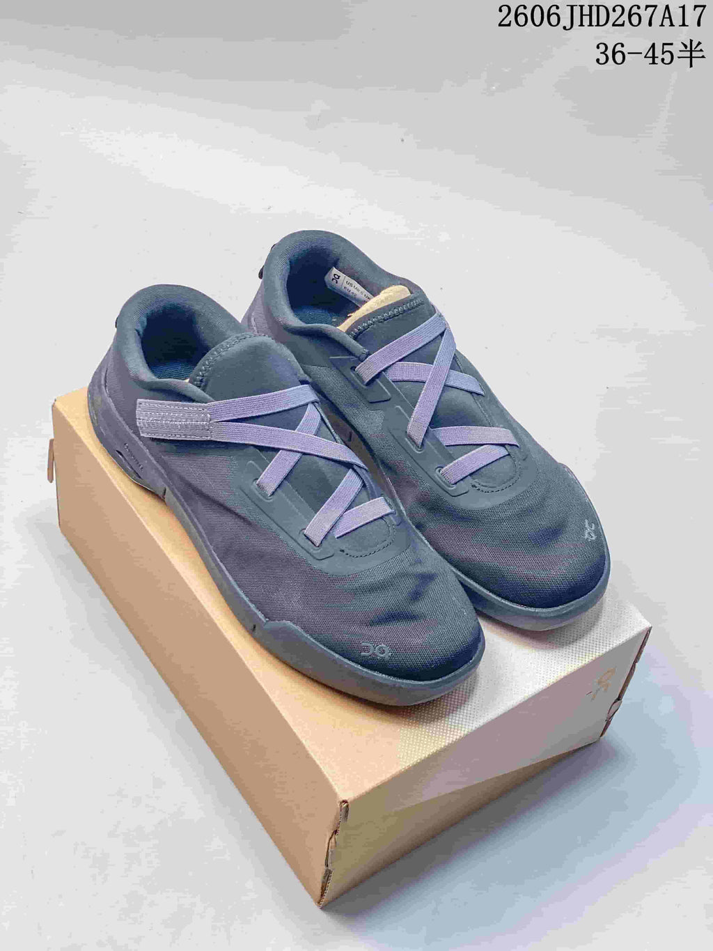 Pair of slate-blue On Cloudnova Moon sneakers with elastic cross-lacing, shown on a box.