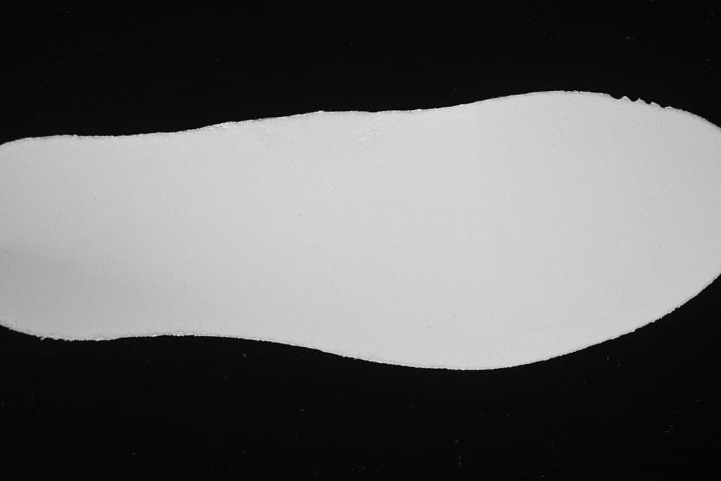 Plain light-colored shoe insole shown separately against a dark background.