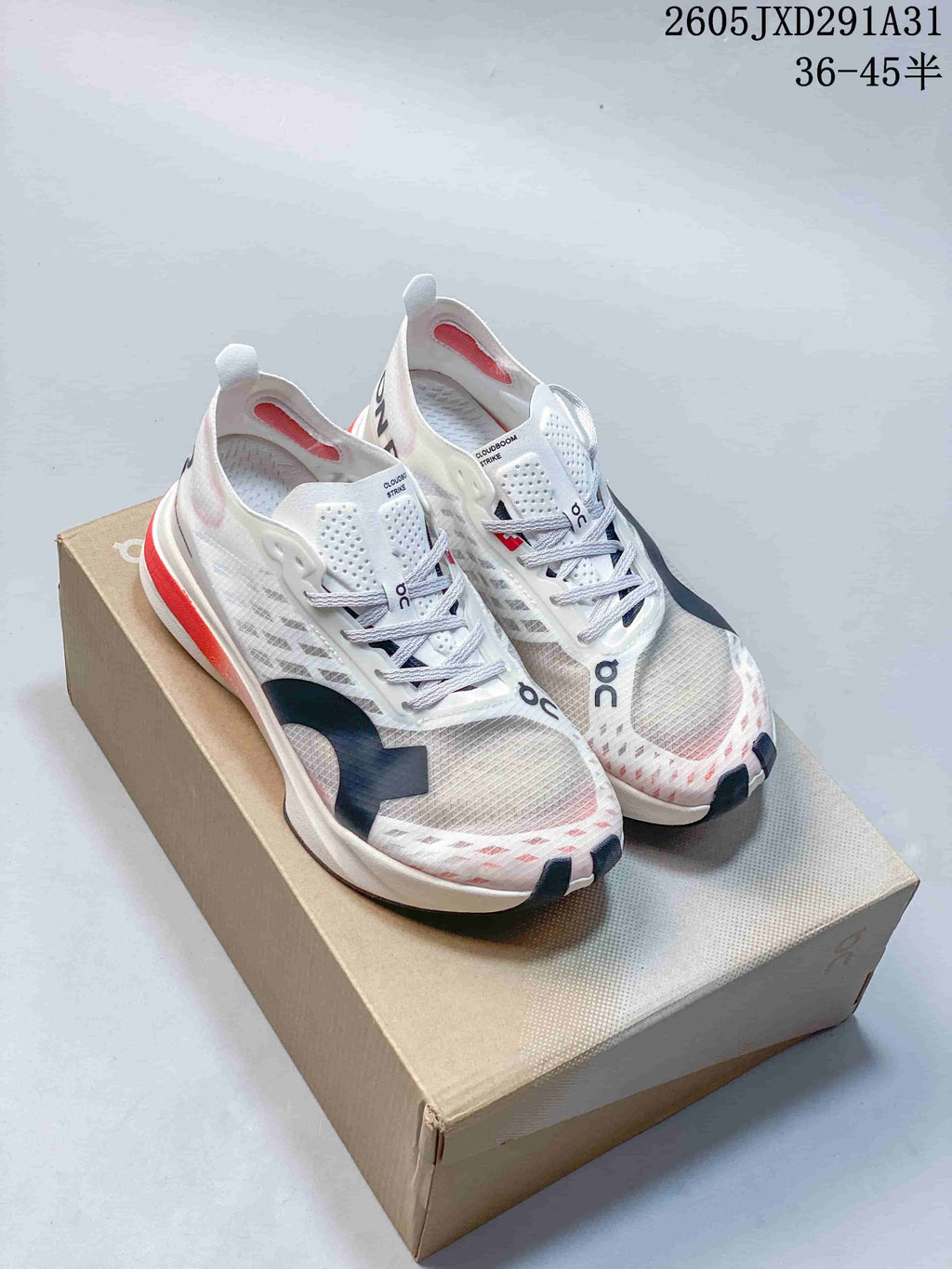 Pair of On Cloudboom Strike shoes in white, gray, navy and coral, shown on a box