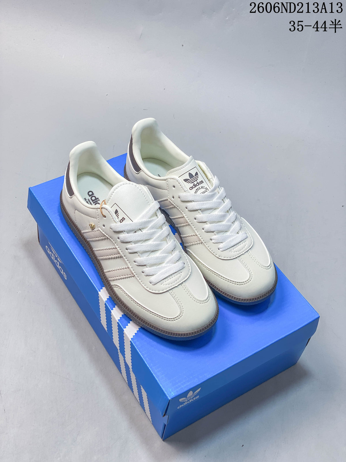 Pair of white adidas Samba OG low-top sneakers with grey accents on a blue shoe box