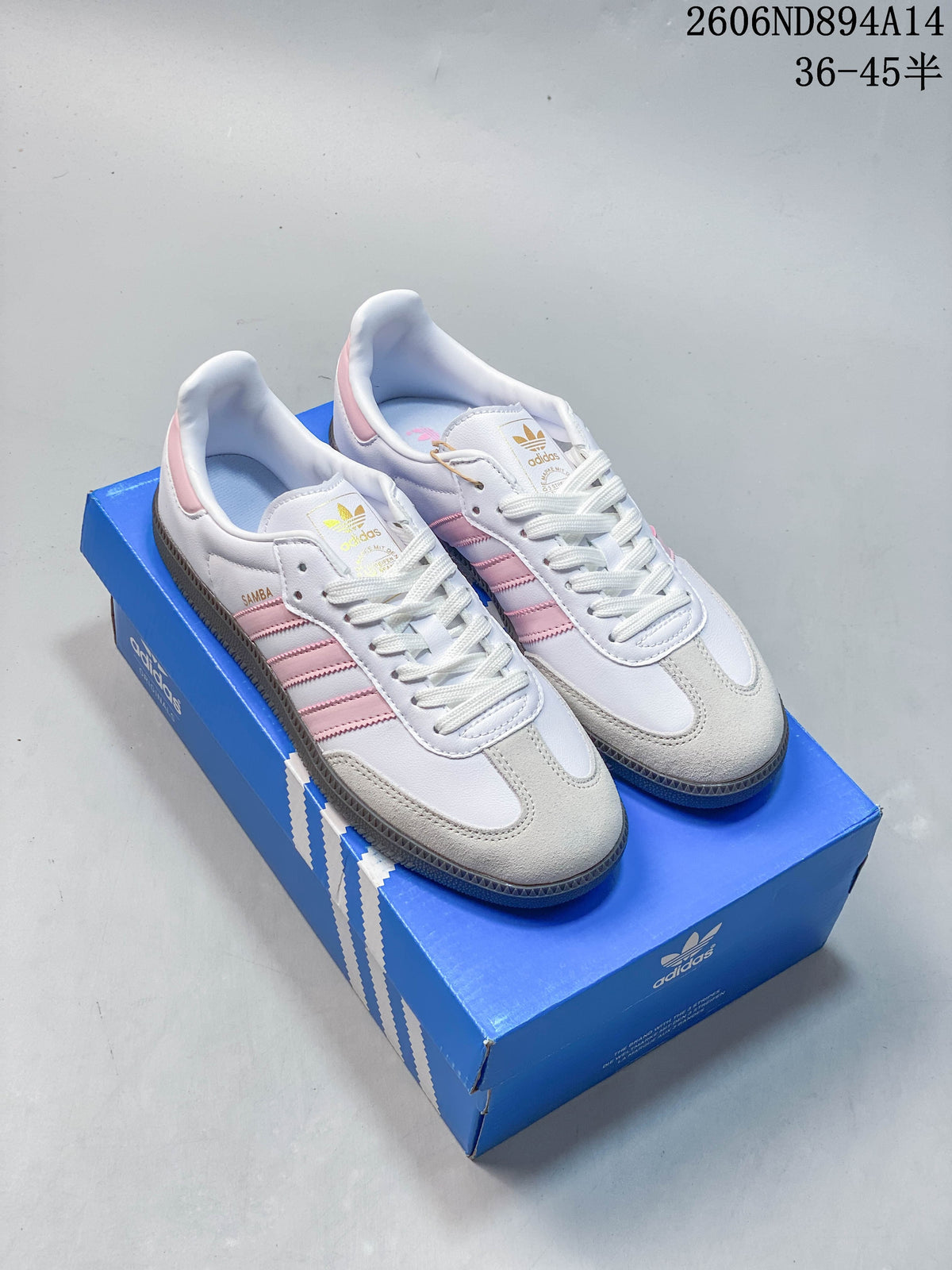 Pair of white adidas Samba OG low-top sneakers with pink stripes and heel details, light beige toe overlays, and dark gum-colored outsoles, shown on a blue shoe box.