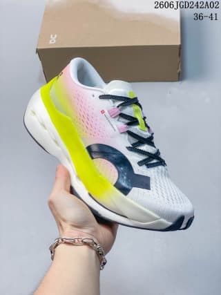 Angled side view of an On Cloudboom Max sneaker showing the white and pink upper, neon yellow midsole accent, black logo detail, and dark outsole.