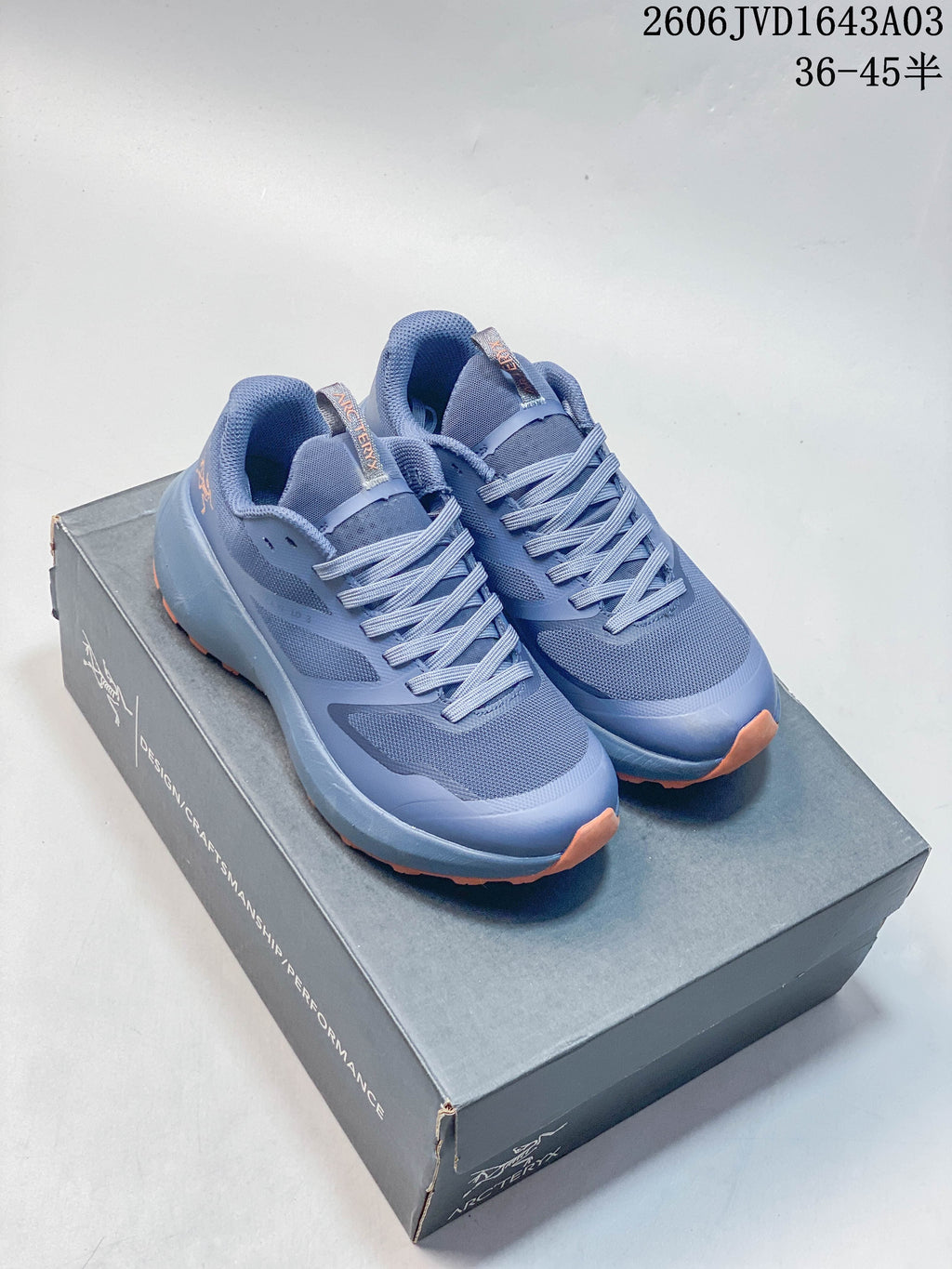 Blue-toned low-top shoes with orange outsole shown on a shoebox