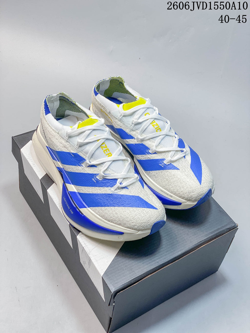 Pair of white Adidas Adizero Prime X3 running shoes with blue stripes and yellow accents, shown from above on a shoe box.