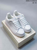 Pair of white Alexander McQueen low-top sneakers with lace-up fronts and chunky soles, displayed on a box.