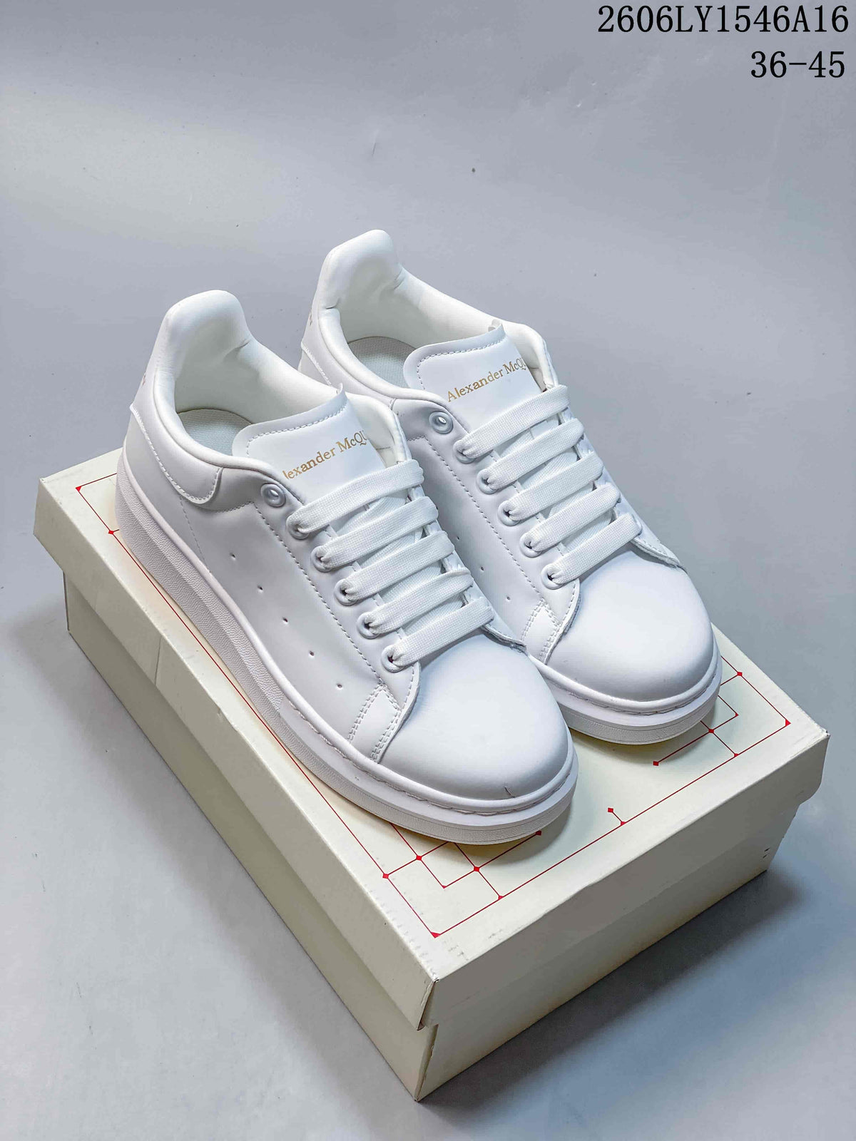 Pair of white Alexander McQueen low-top sneakers with lace-up fronts and chunky soles, displayed on a box.