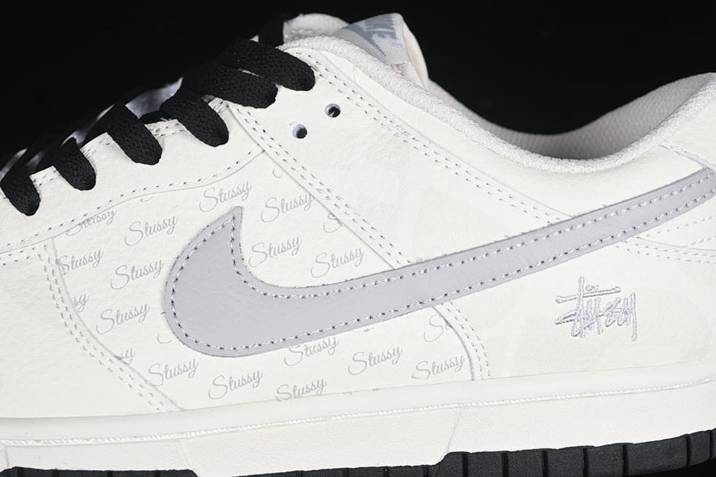Close-up of the grey Swoosh, repeating Stüssy script, black laces and side branding.