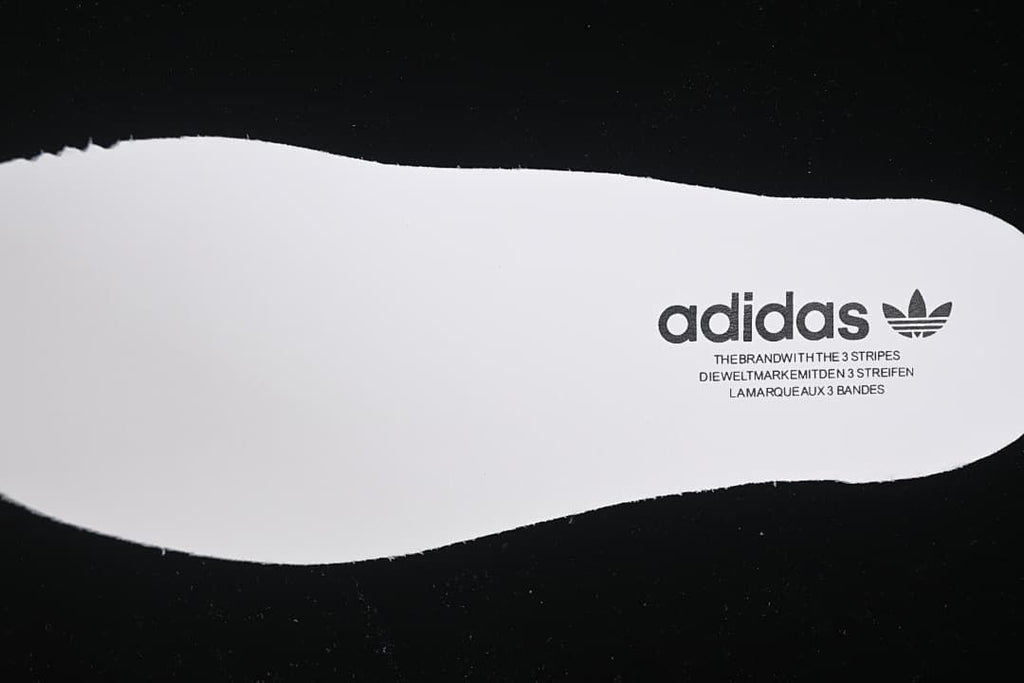 White shoe-shaped cutout with adidas branding against a black background