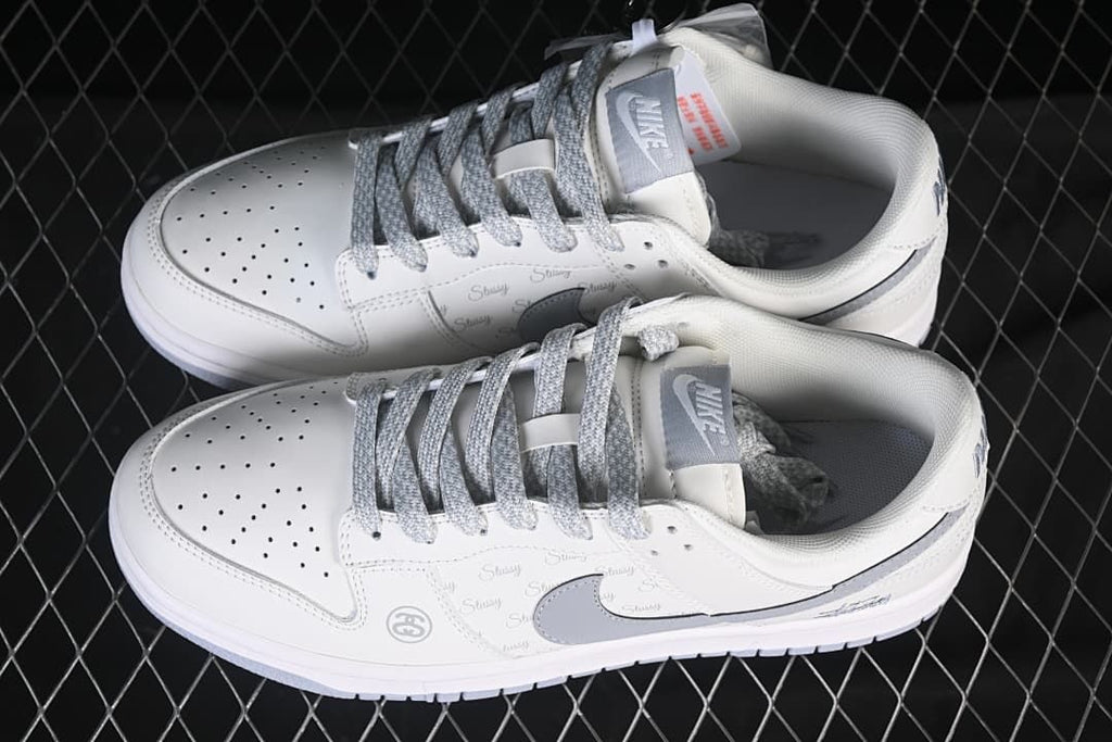 Top view of a pair of white Nike SB Dunk low-top sneakers with grey laces, grey Swooshes and printed side panels.