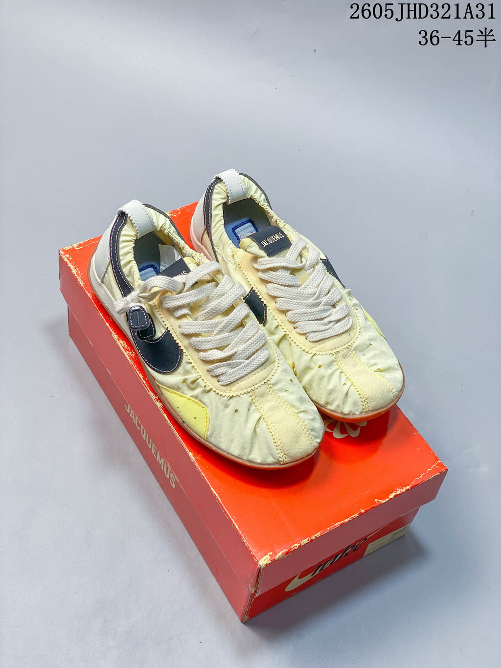 Pair of pale yellow Nike x Jacquemus Moon Shoe SP sneakers on a red shoebox