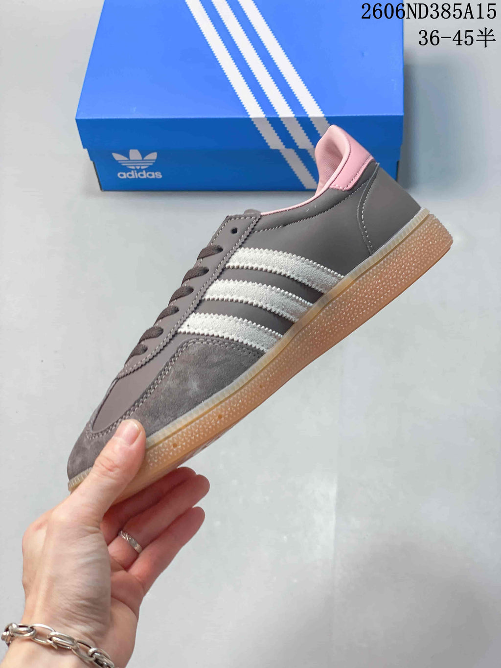 Side profile of the grey sneaker showing white stripes, pink collar details and gum-colored sole.