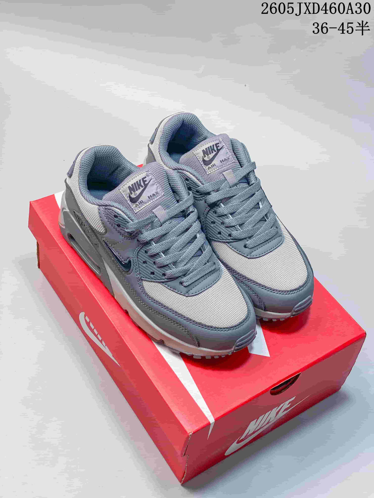 Pair of grey Nike Air Max 90 sneakers displayed on a red shoe box
