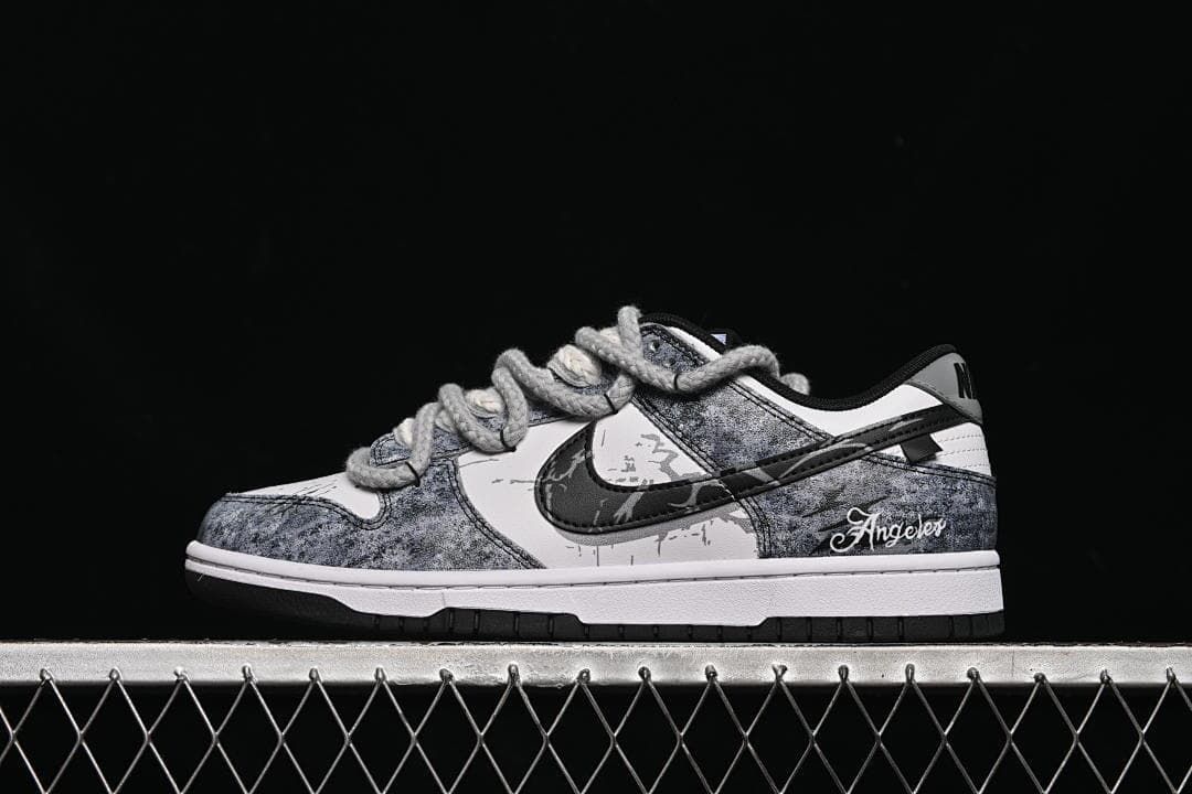 Side view of a grey, black, and white Nike SB Dunk Low sneaker with thick grey laces and “Angeles” heel embroidery