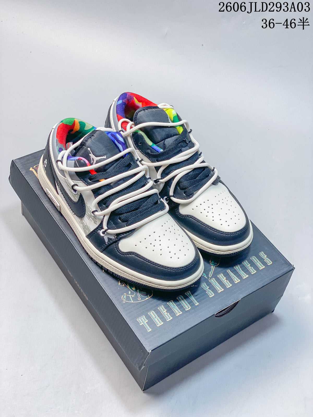 Pair of white and navy low-top Jordan sneakers with colorful lining, shown on a graphic shoebox
