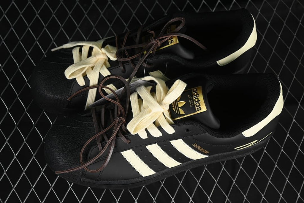 Pair of black and cream adidas Superstar sneakers with contrasting laces.
