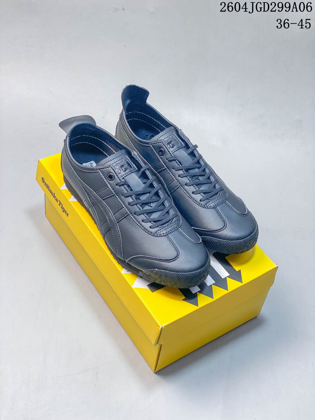 Pair of charcoal gray Onitsuka Tiger Mexico 66 SD sneakers on a yellow shoebox