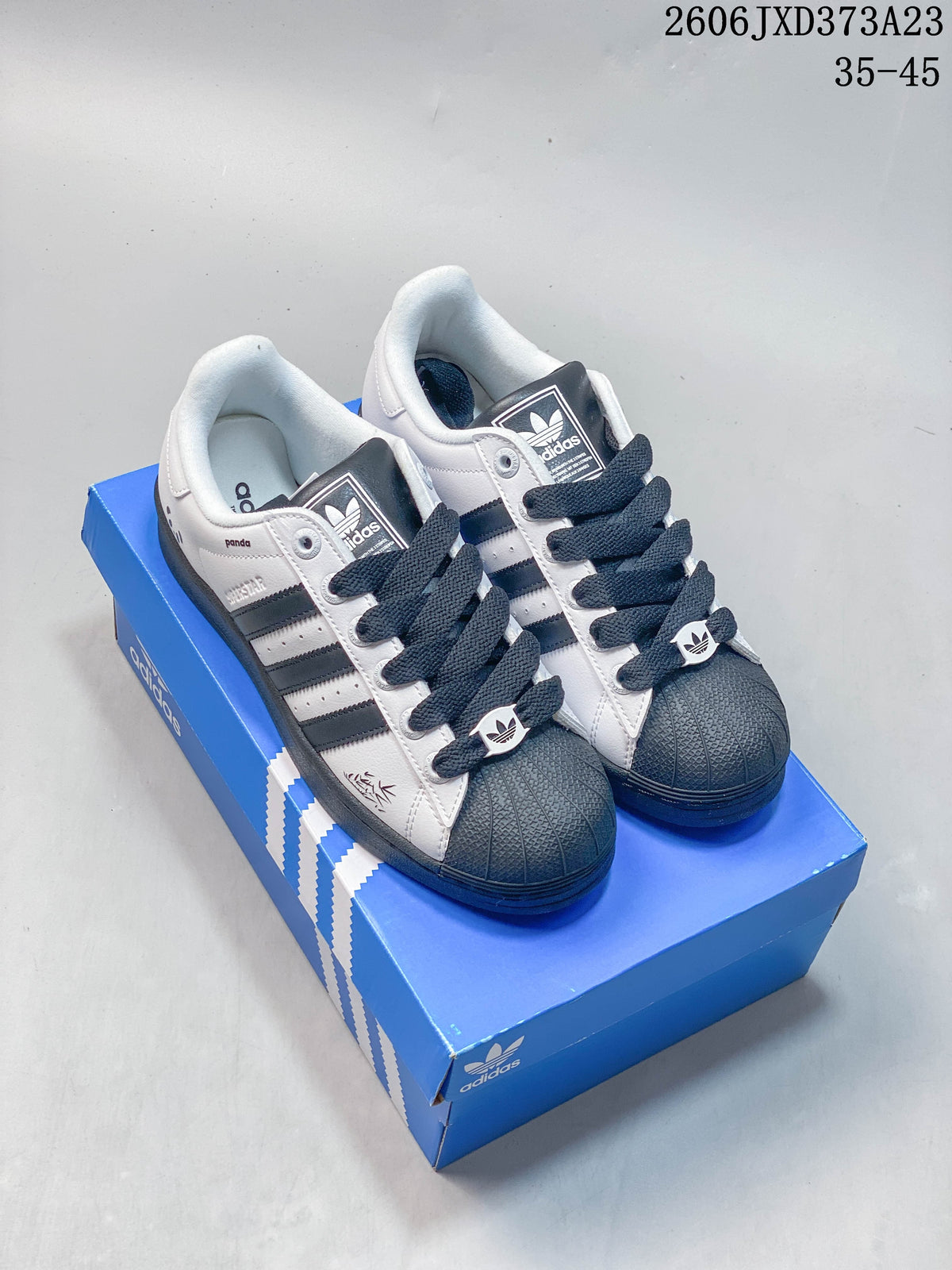 Pair of white and black Adidas Originals Superstar sneakers with dark shell toes and laces on a blue shoe box