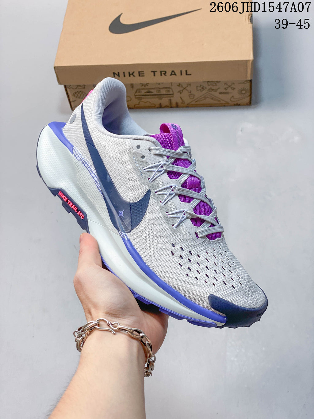 Close side view of a gray Nike ReactX Pegasus Trail 5 shoe with a dark blue Swoosh and pink accents.