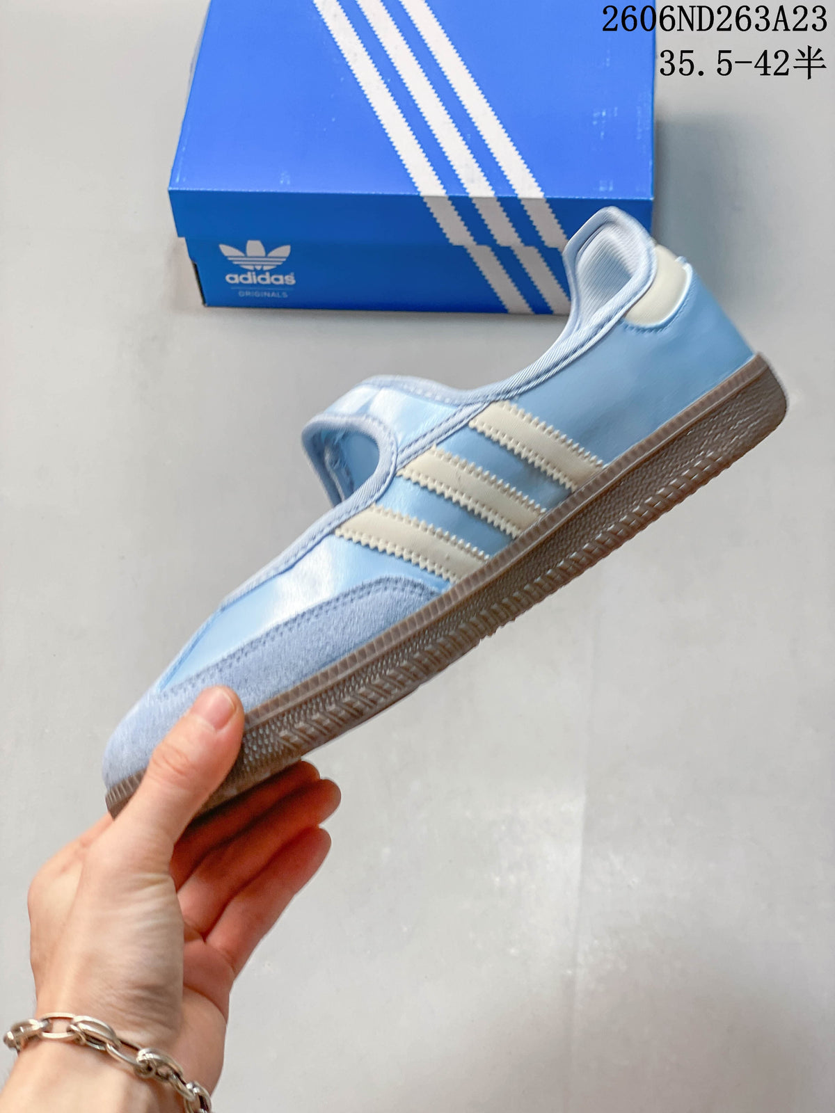 Side profile showing the strap, cream stripes and brown outsole of a light blue Adidas Samba Jane
