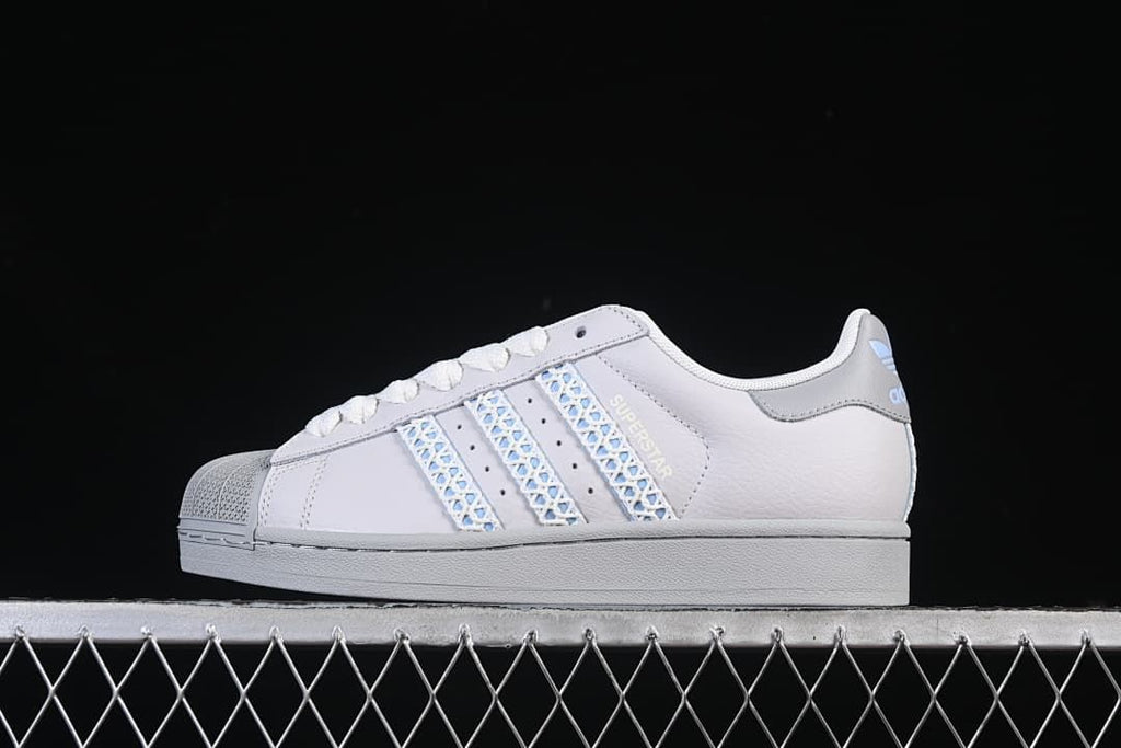 Side view of a white adidas Superstar II sneaker with pale blue patterned stripes and a grey sole.