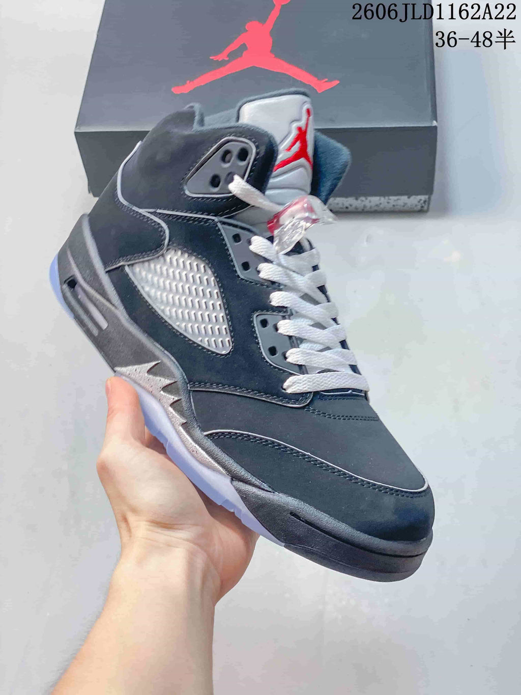 Angled side view of a dark high-top sneaker with a silver-toned side panel, white laces and red tongue detail.