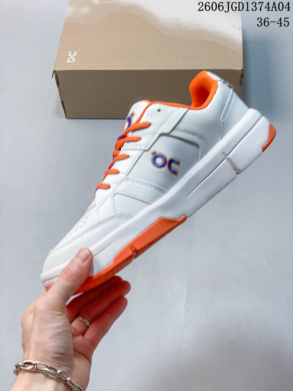 Side profile of the white court-style sneaker with orange outsole accents and blue-orange logo detail