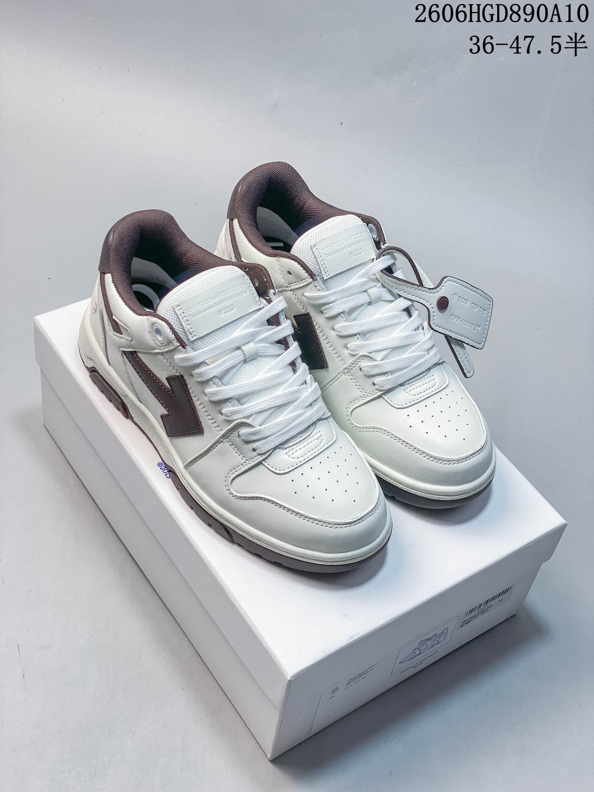 Pair of white low-top sneakers with dark brown accents and Arrow-style side panels, shown on a box.