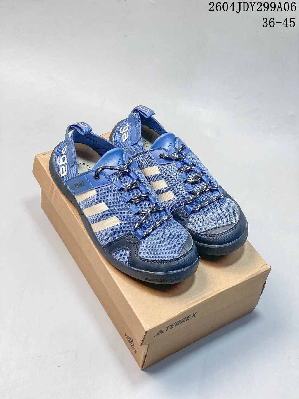 Pair of blue Adidas outdoor shoes with cream side stripes and cord-style laces, shown on a box