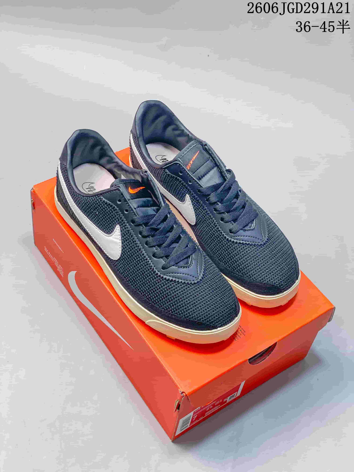 Dark navy Nike Astrograbber Leather low-top sneakers with light-colored Swoosh logos and outsole, photographed on an orange shoebox.