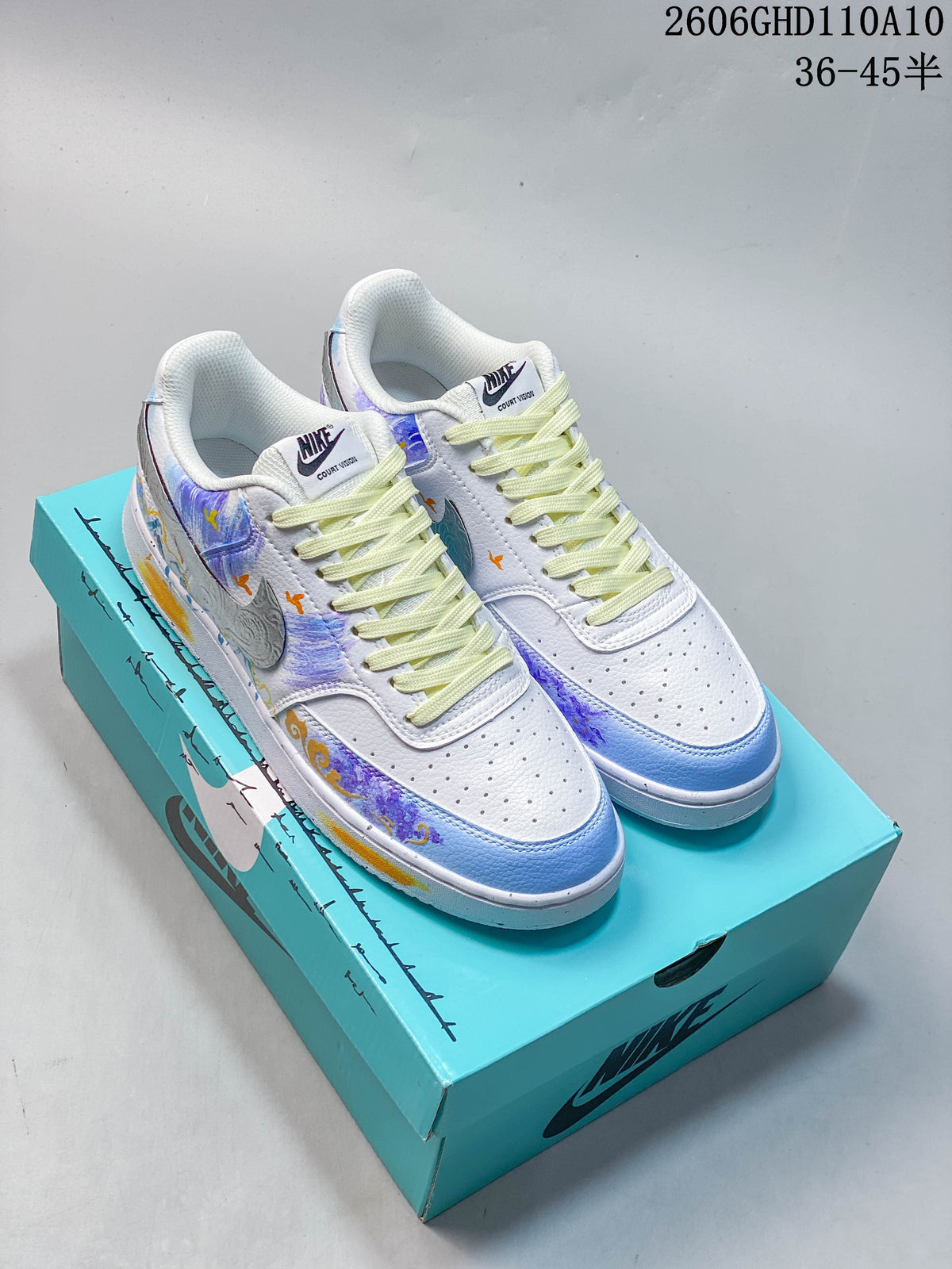 Pair of white Nike Court Vision low-top sneakers with blue, purple, and orange decorative details, displayed on a turquoise shoe box.