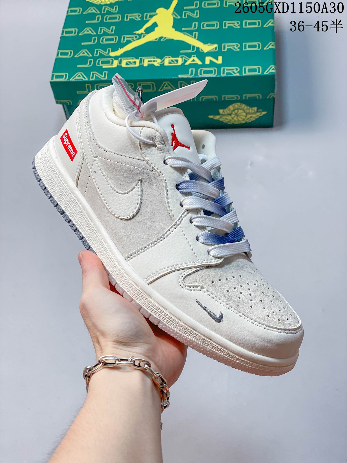 Angled side view showing off-white and gray panels, blue-and-white laces, red heel label, and a small charm.