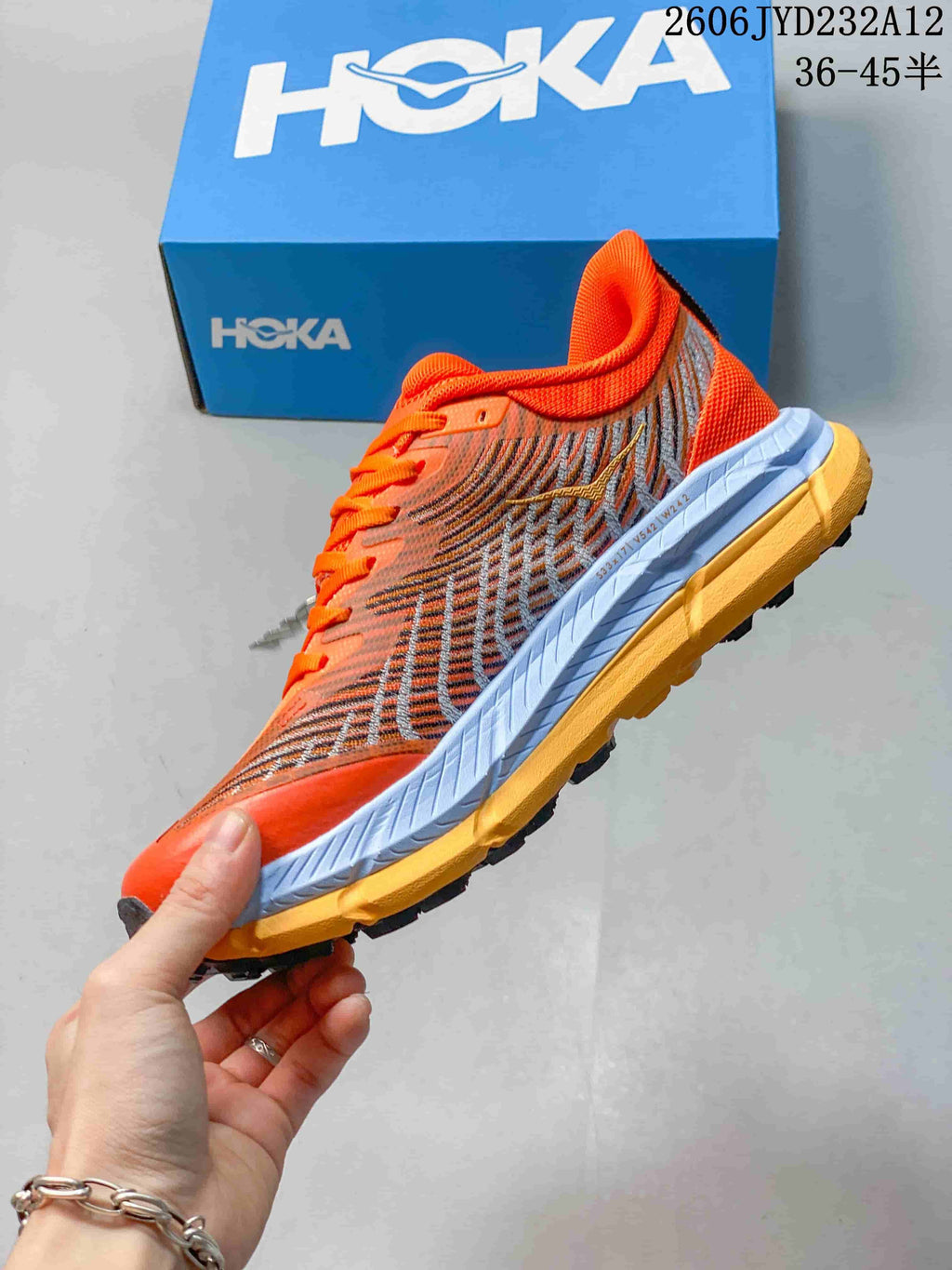 Side view of the orange HOKA shoe with patterned panels and a lugged outsole