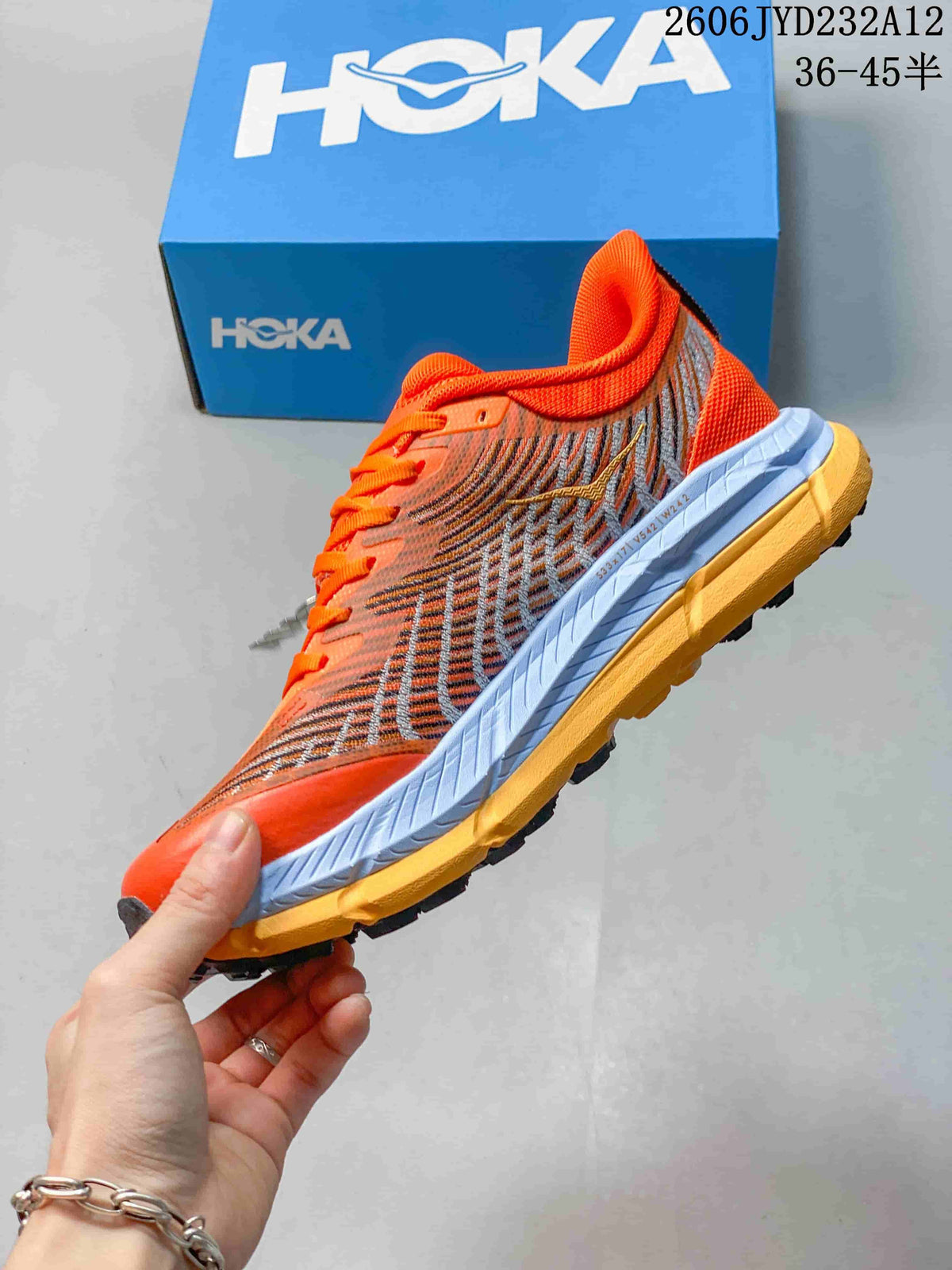 Side view of the orange HOKA shoe with patterned panels and a lugged outsole