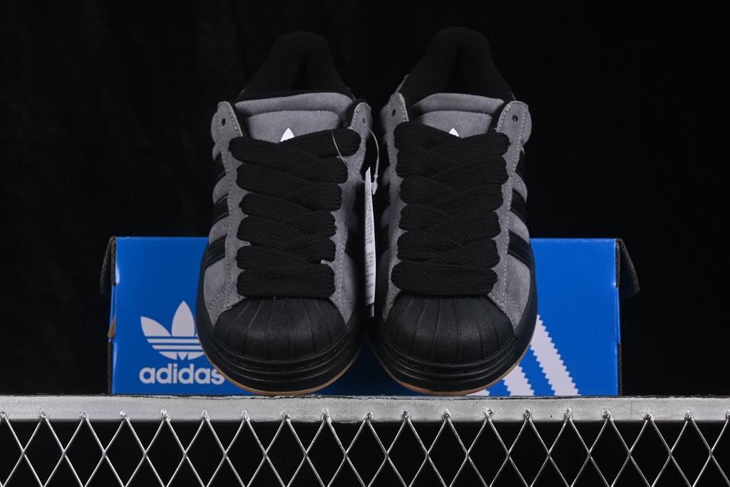 Front view of grey and black Adidas Superstar 2 ST sneakers positioned on a blue shoebox.