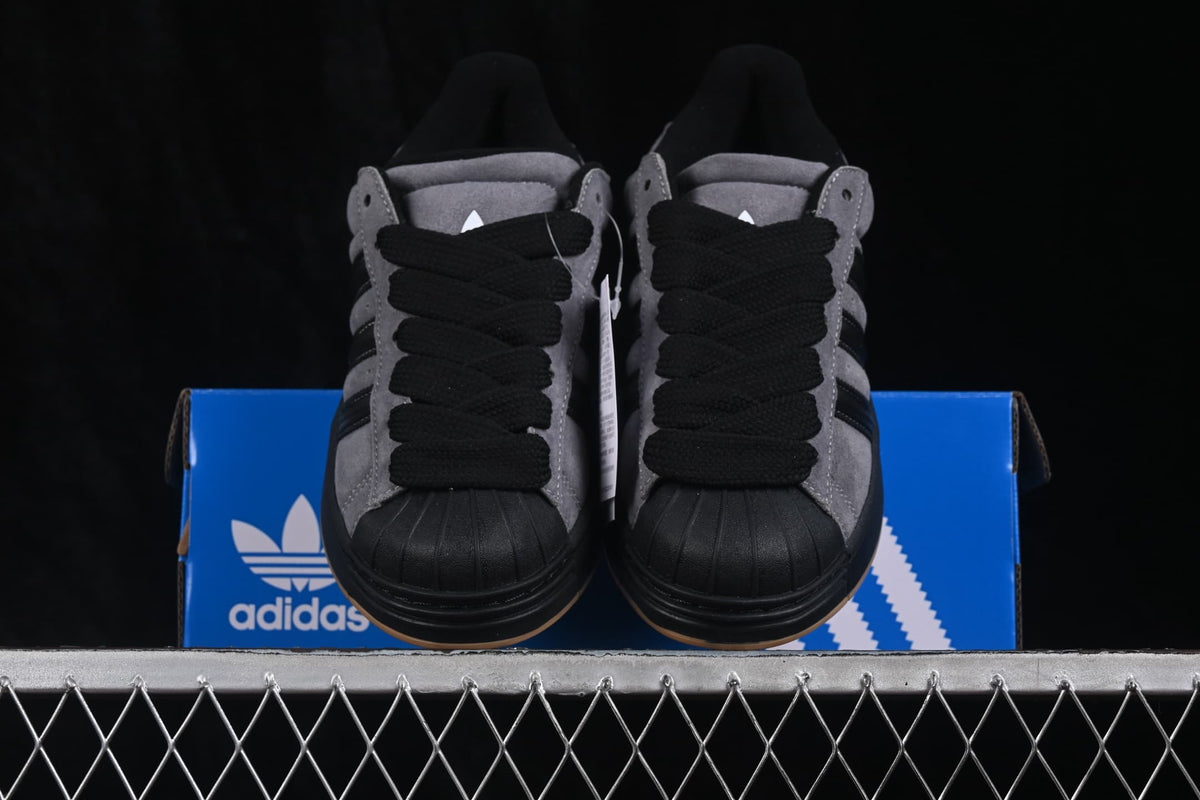 Front view of grey and black Adidas Superstar 2 ST sneakers positioned on a blue shoebox.