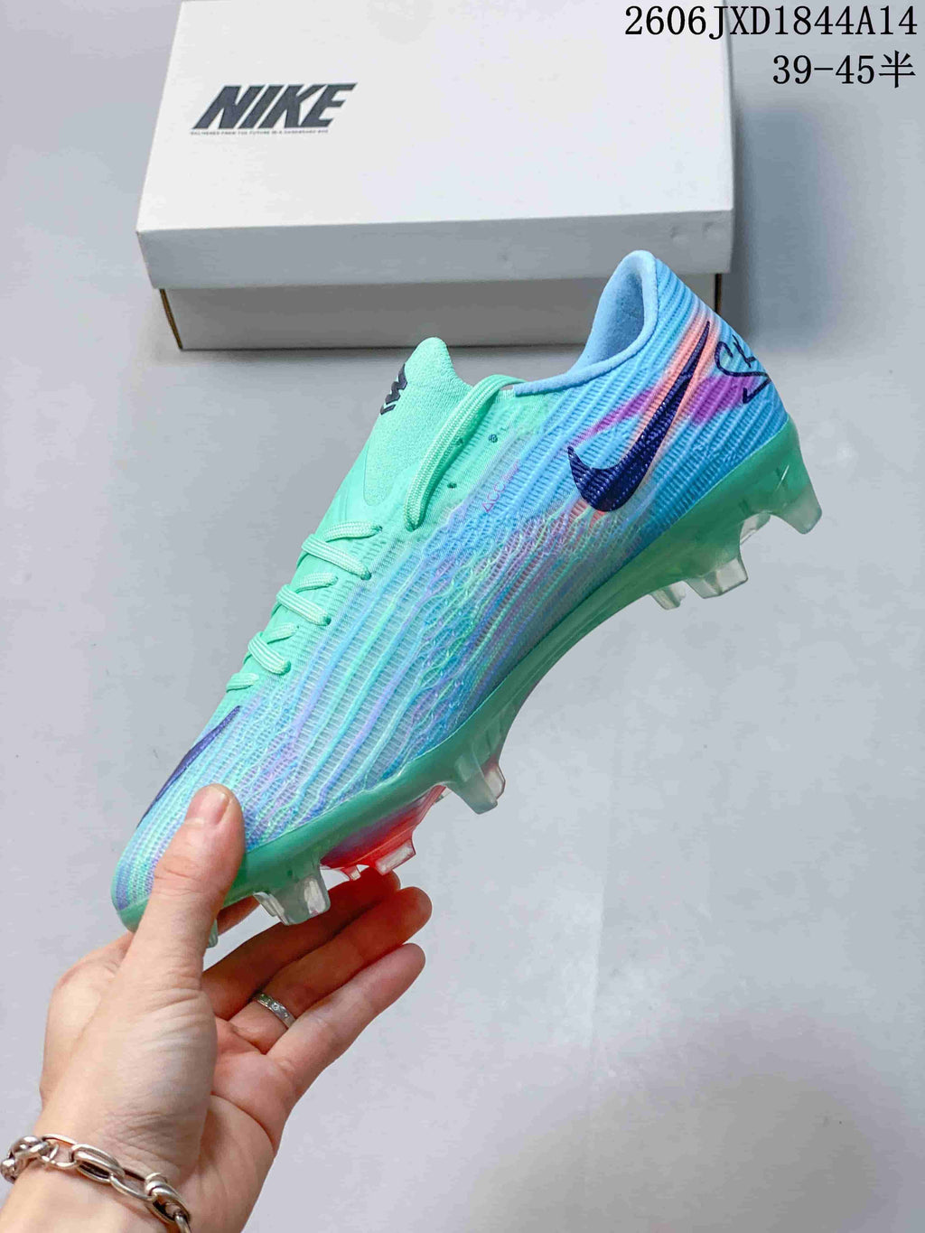 Side profile of a mint and aqua soccer cleat with blue and coral accents and a studded outsole.