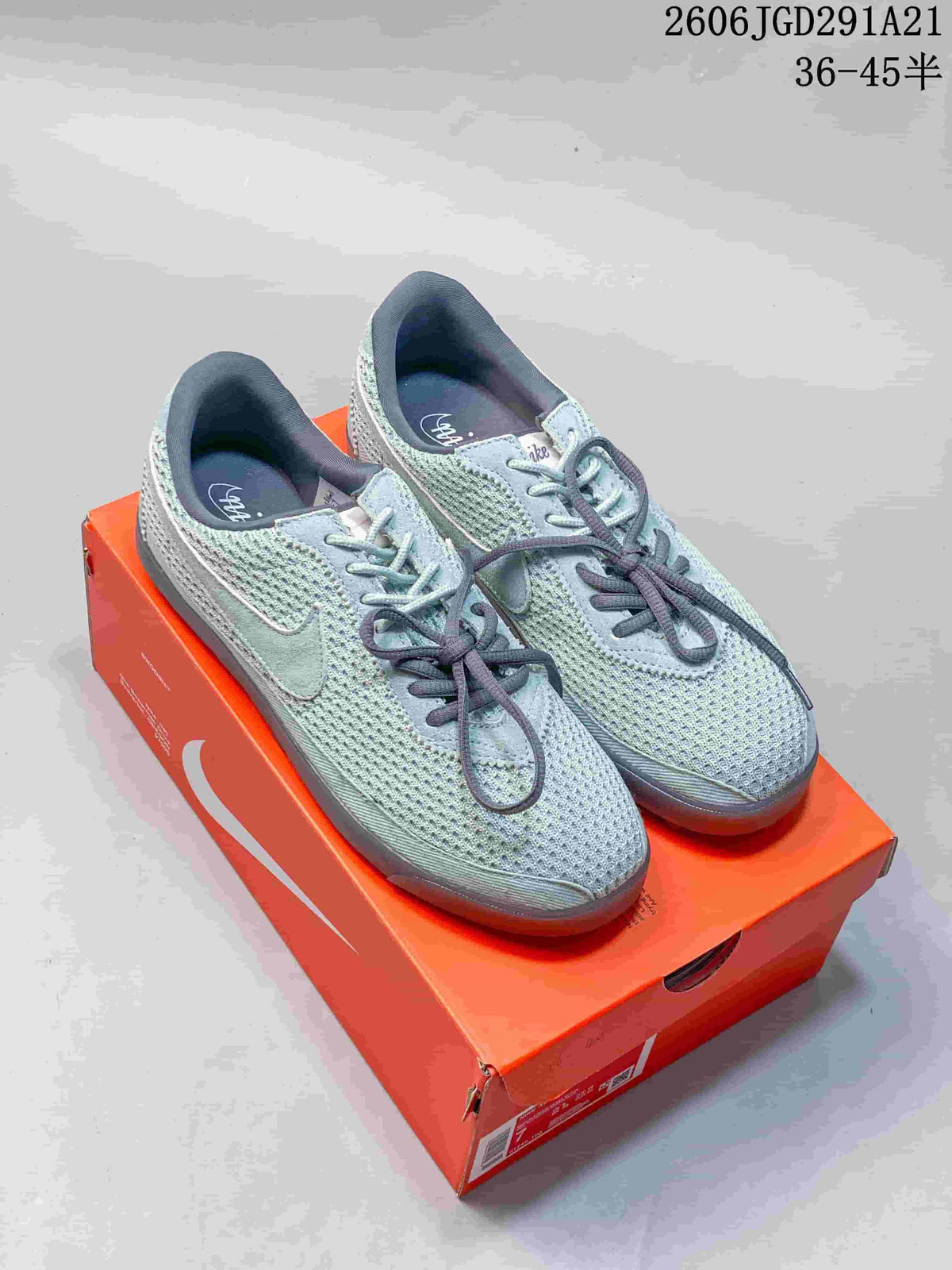 Pale blue-gray Nike low-top sneakers with a perforated-looking upper and darker laces, photographed on an orange shoebox.