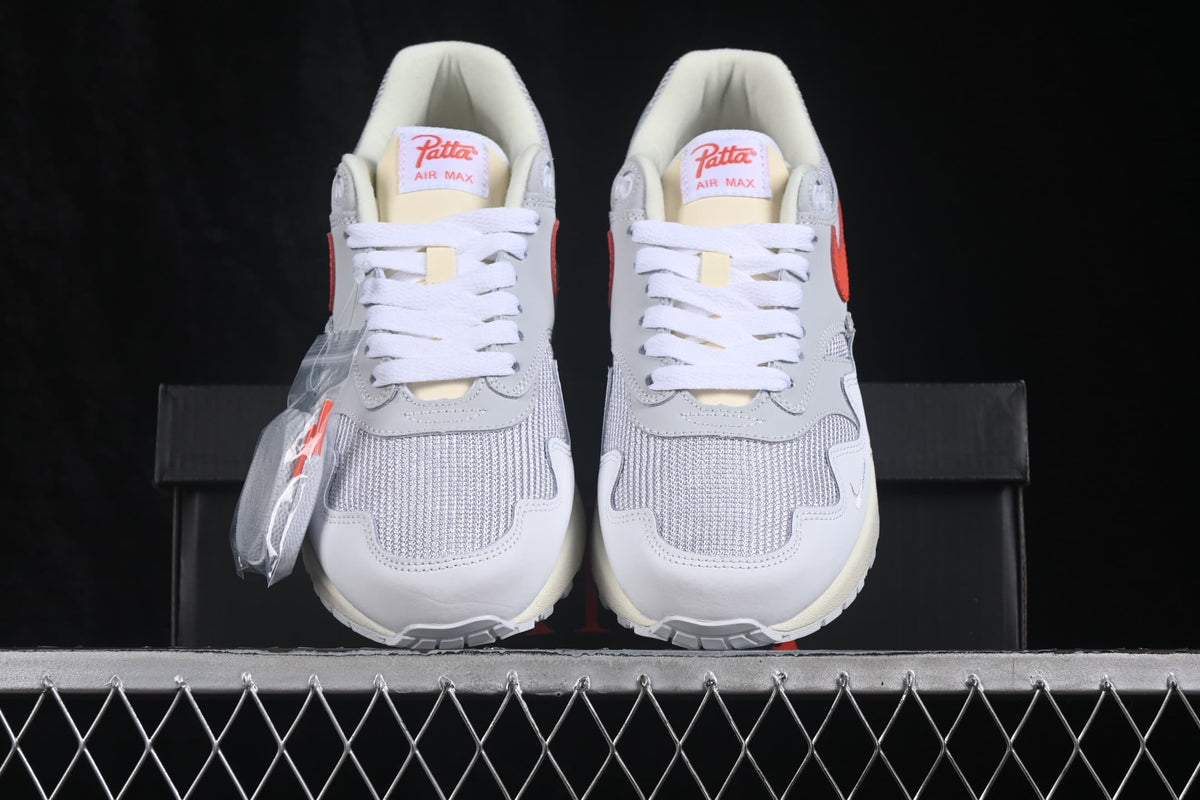 Front view of the pair displayed on the shoebox, showing white laces, grey mesh toe boxes, orange Swooshes, and Patta tongue labels.