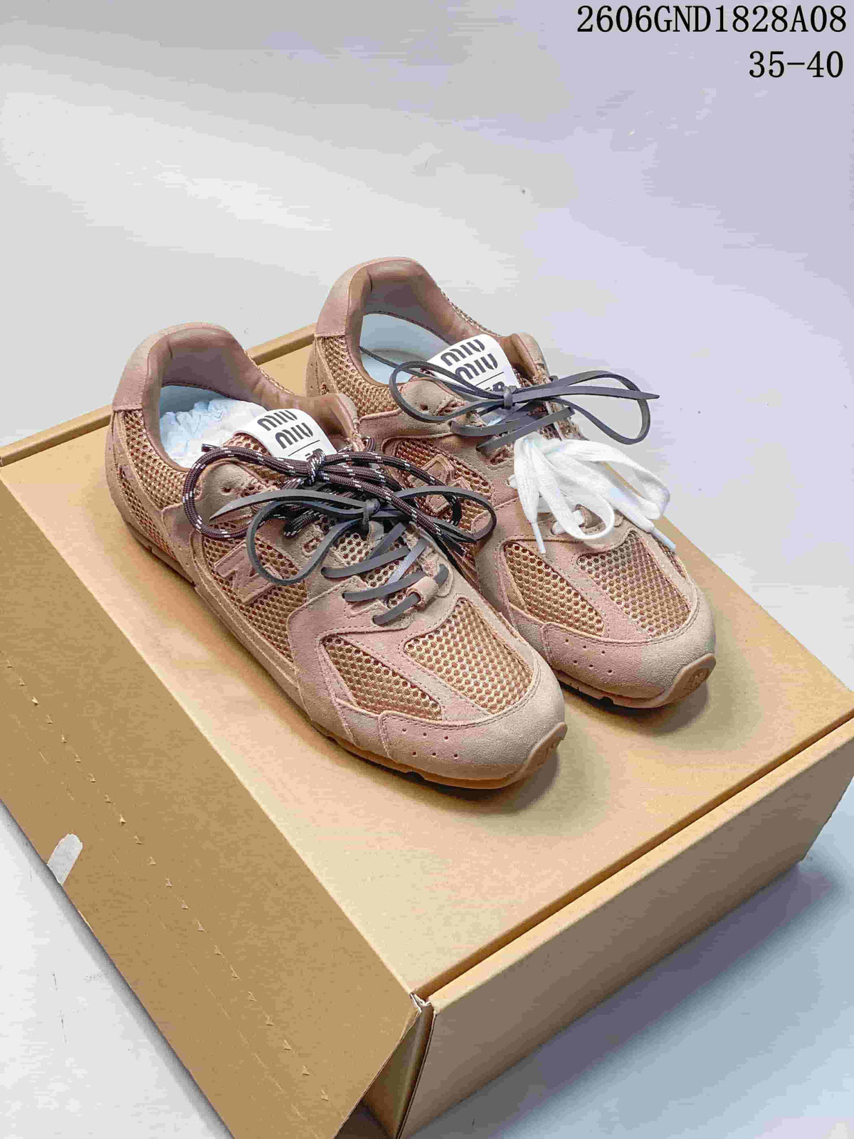 Pair of rose-beige Miu Miu and New Balance-style sneakers with mixed-color laces, shown on a box.