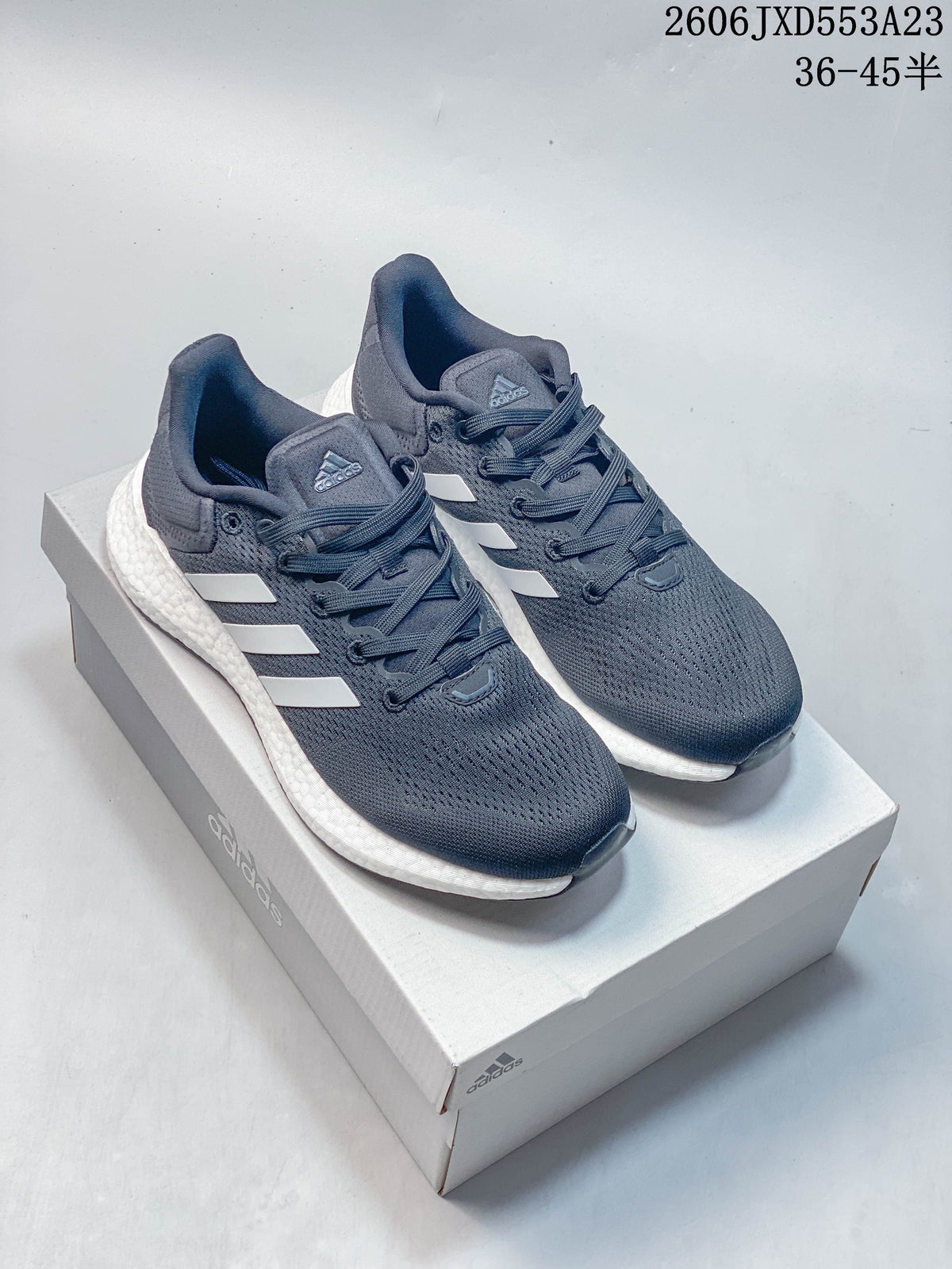 Pair of navy Adidas PureBoost 21 running shoes with white stripes and textured white midsoles on a shoebox.