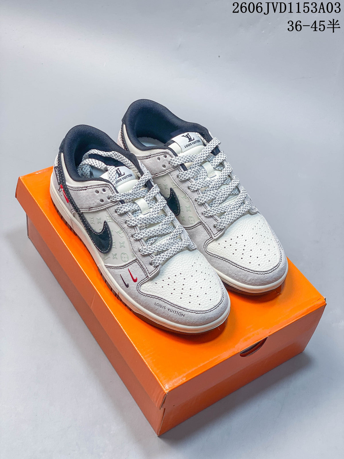 Pair of white and light gray low-top sneakers with dark navy accents on an orange box