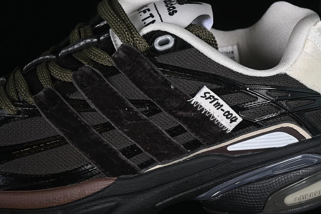 Close-up of the black upper, layered side panels, olive-toned laces and SFTM detail.