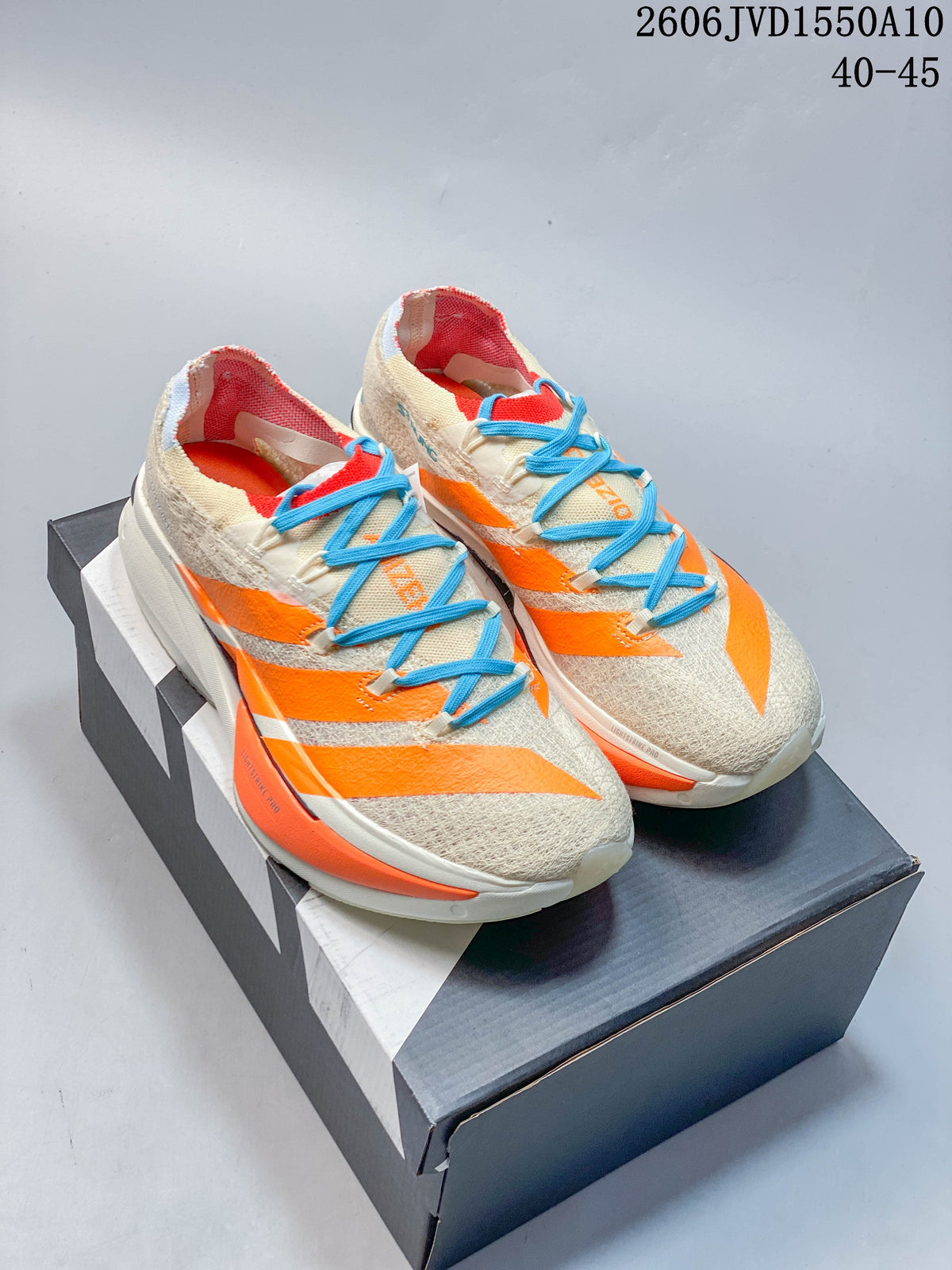 Pair of cream Adidas Adizero Prime X3 running shoes with orange accents and blue laces, shown on a box.